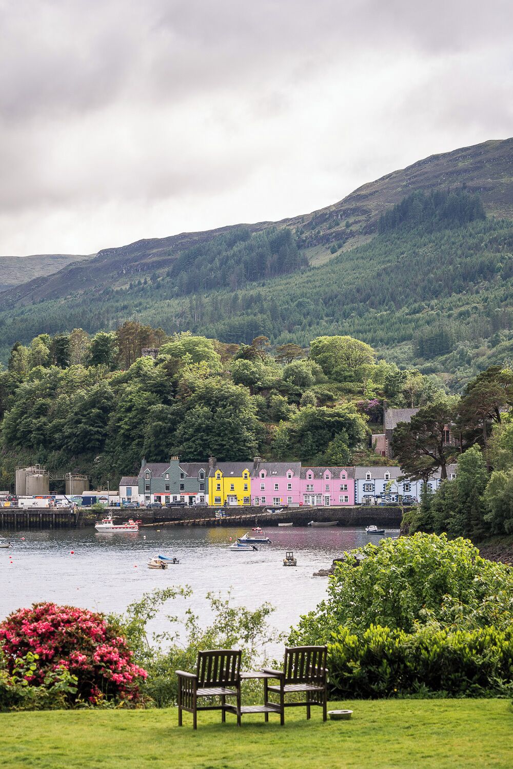 A coastal town with colorful buildings, a grassy area with benches, and boats on the water.