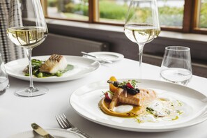 A dining table with plates of food, wine glasses, and cutlery.