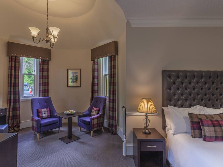 A bedroom with a large bed, two chairs, a table, and a nightstand.