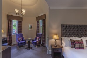 A bedroom with a large bed, two chairs, a table, and a nightstand.
