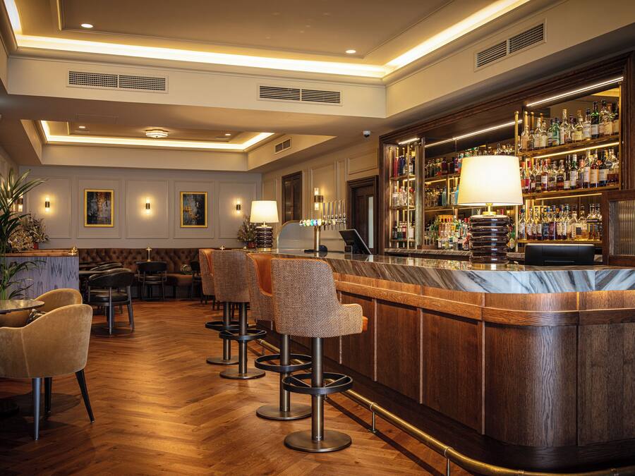 Angolo bar con pavimento in legno, sgabelli da bar e una scaffalatura fornita di liquori.