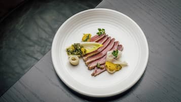 Ein weißer Teller mit geschnittenem Fleisch, Gemüse und einem kleinen weißen Gegenstand auf einem dunklen Holztisch.