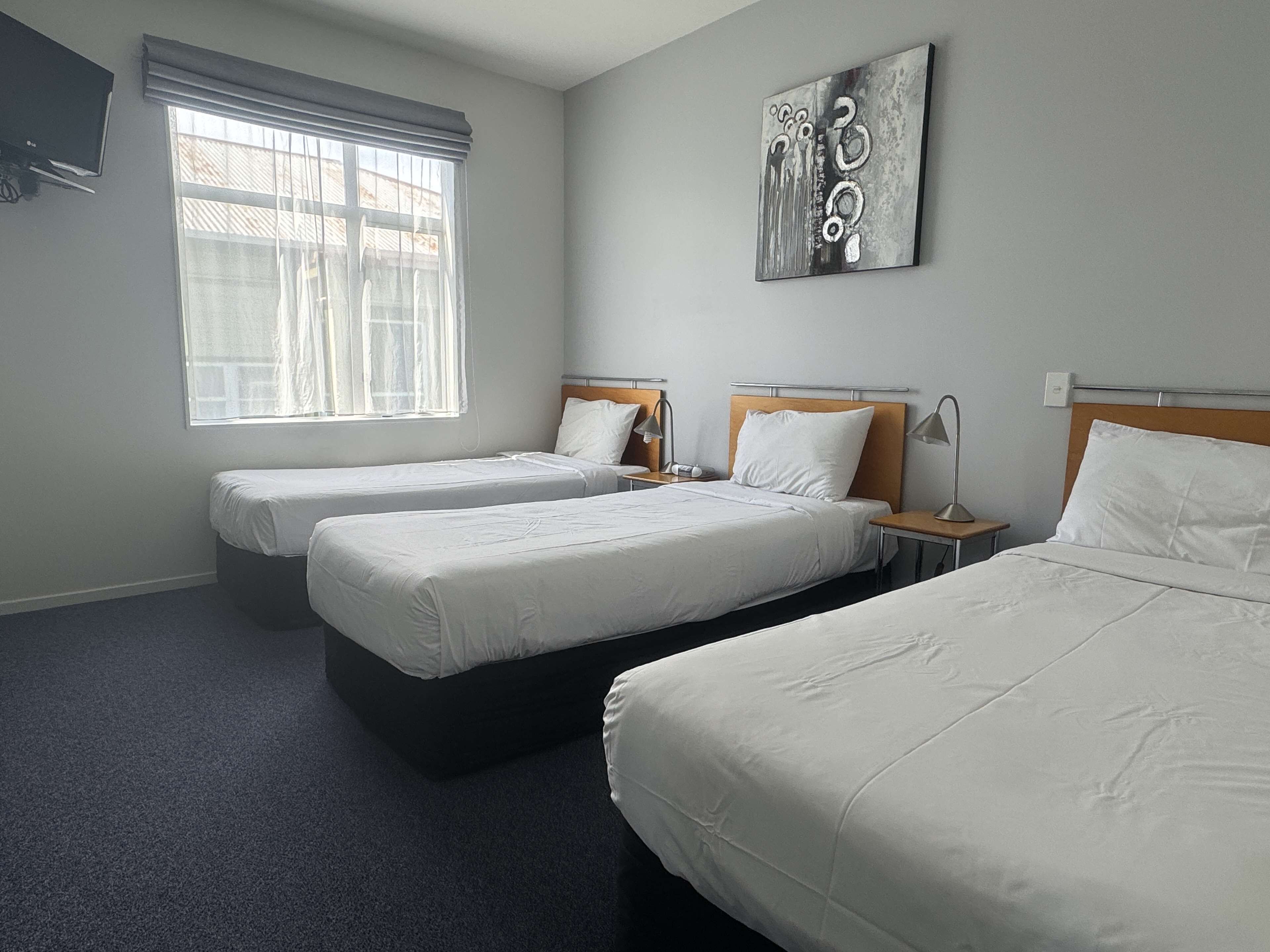 Une chambre d’hôtel avec deux lits simples, une grande fenêtre avec des rideaux, une œuvre d’art accrochée au mur et un téléviseur à écran plat.