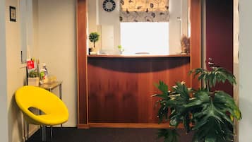 A reception area with a wooden reception desk, a clock, a potted plant, and a yellow chair.
