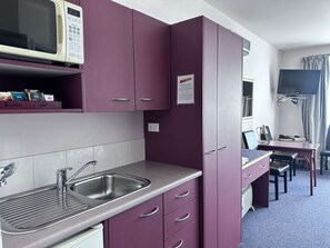 A compact kitchen with a microwave, sink, and cabinets. There is a small dining area with a table and chairs. - Best Western Wellington (Wellington)