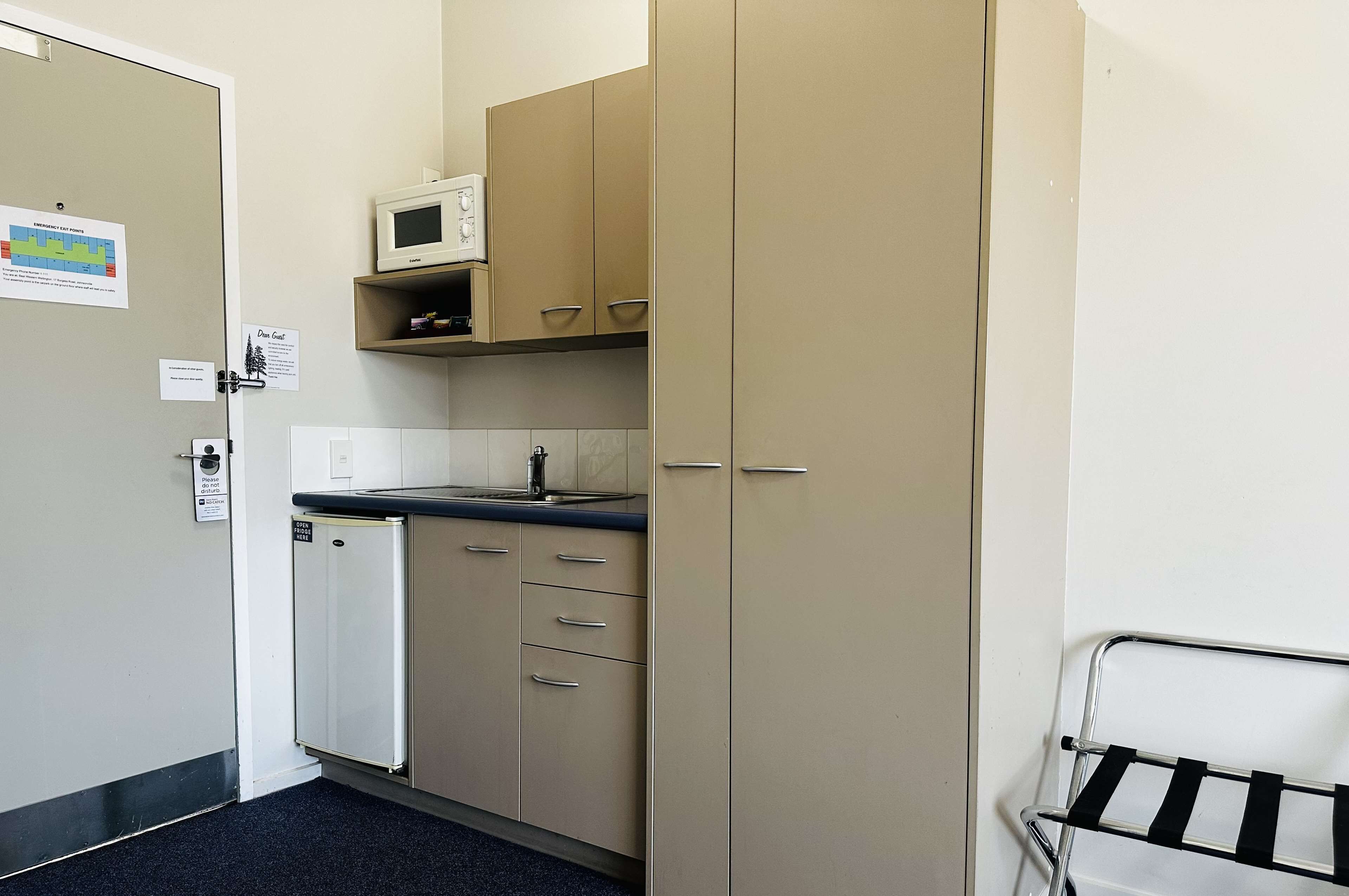 A compact kitchenette with a microwave, a small refrigerator, and a sink. There are cabinets with drawers and a metal rack for hanging items.