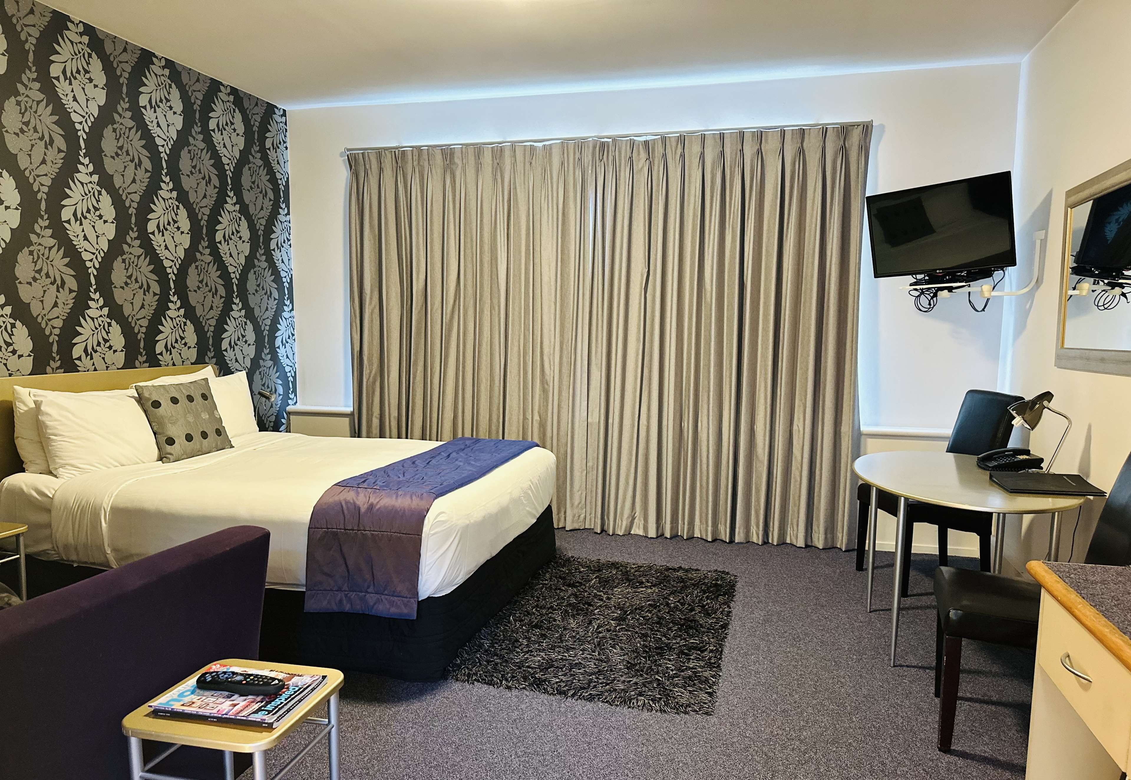 A hotel room with a bed, a desk, a chair, a TV, and a window with curtains.