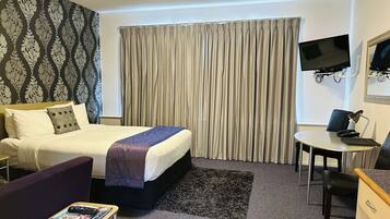 A hotel room with a bed, a desk, a chair, a TV, and a window with curtains.