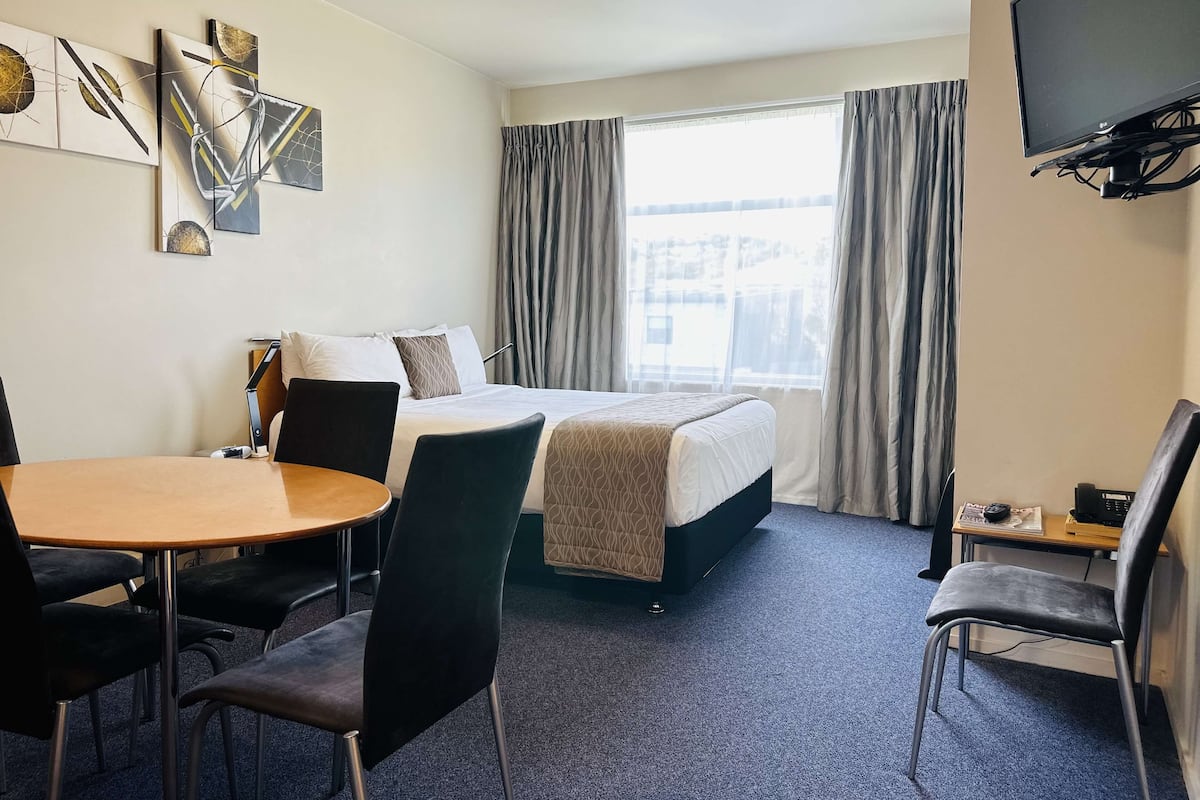A hotel room with a bed, a desk, a chair, a TV, and artwork on the wall.