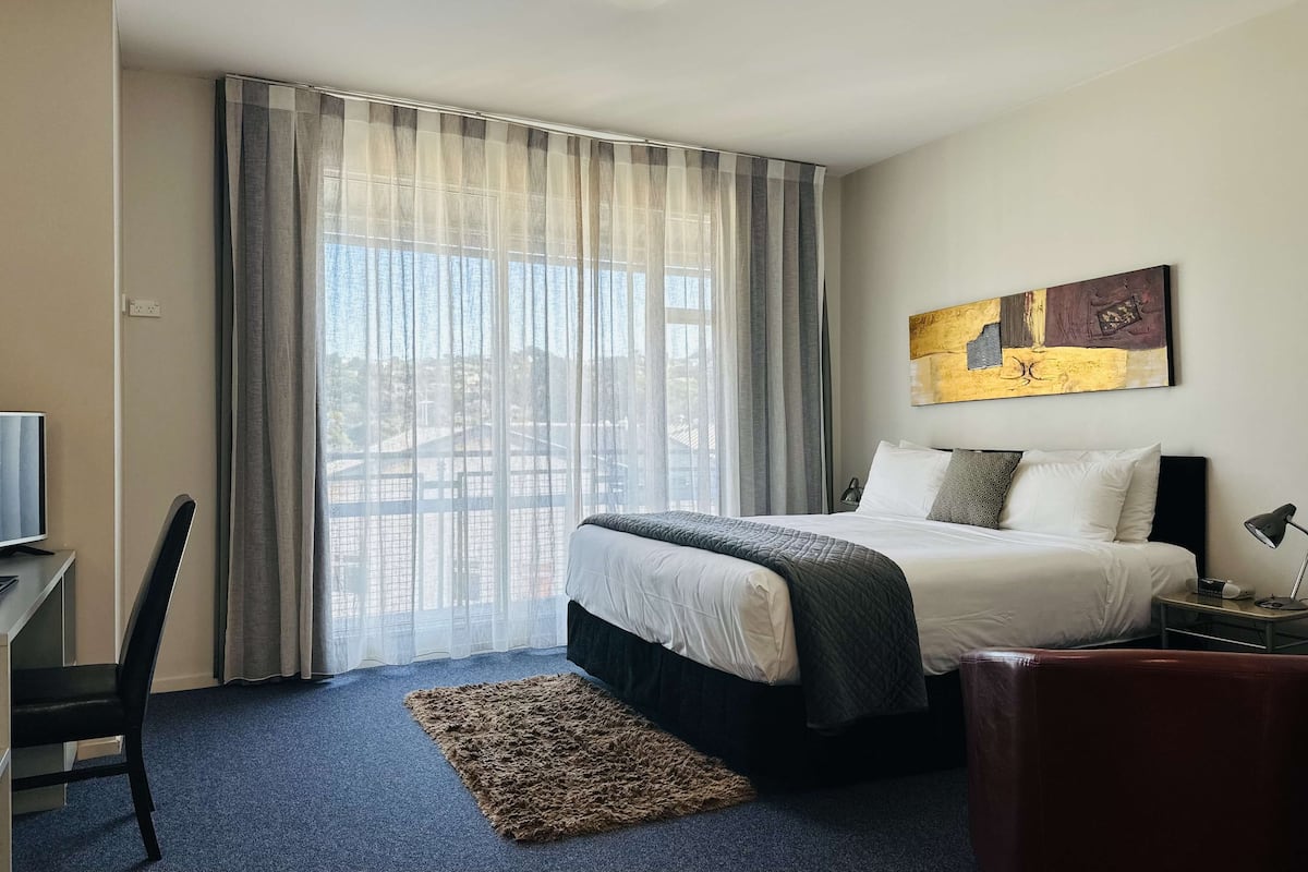 A hotel room with a large bed, a desk, a chair, a TV, and a painting on the wall.