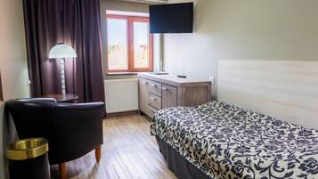 Un dormitorio con cama, escritorio, silla, lámpara y televisor.