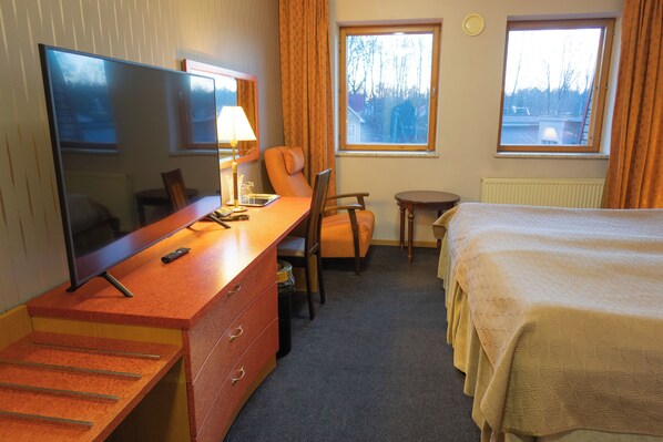 A hotel room with a bed, a desk with a TV, a chair, a small table, and two windows with curtains. - Tahetorni Hotel (Tallinn)