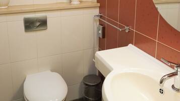 Une salle de bain avec des toilettes, un lavabo et un miroir. On y trouve des serviettes et un pichet en verre accroché au mur.