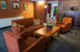 Vestíbulo de hotel con pared de ladrillo, cuadros enmarcados, sofá de madera, mesa de centro de madera y lámpara de pie.