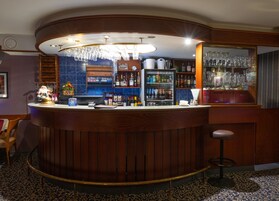 Una zona de bar con una barra curva, un minibar y una variedad de botellas y vasos.