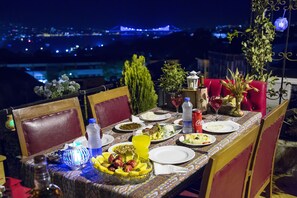 Mesa servida con platos, vasos y un frutero, con vistas a un paisaje urbano de noche.