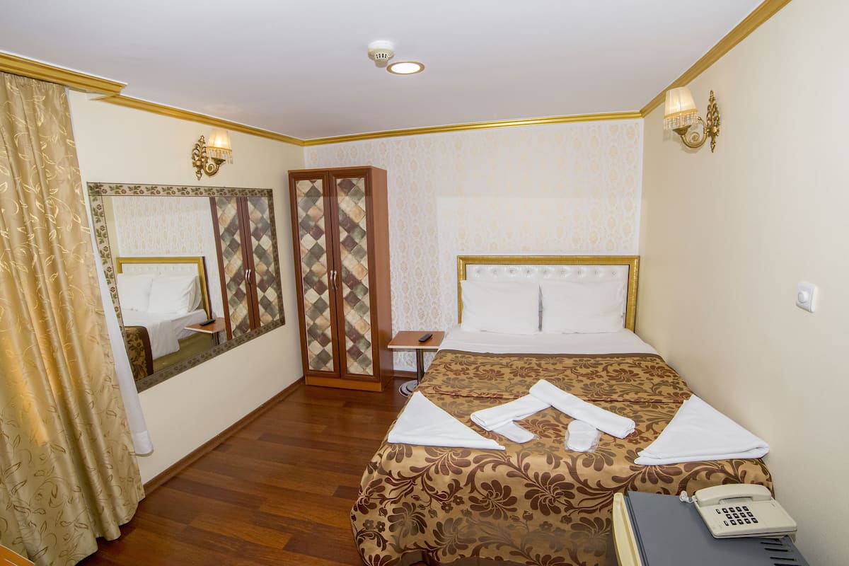 Quarto de hotel com cama, telefone, espelho, guarda-roupa e uma pequena mesa.