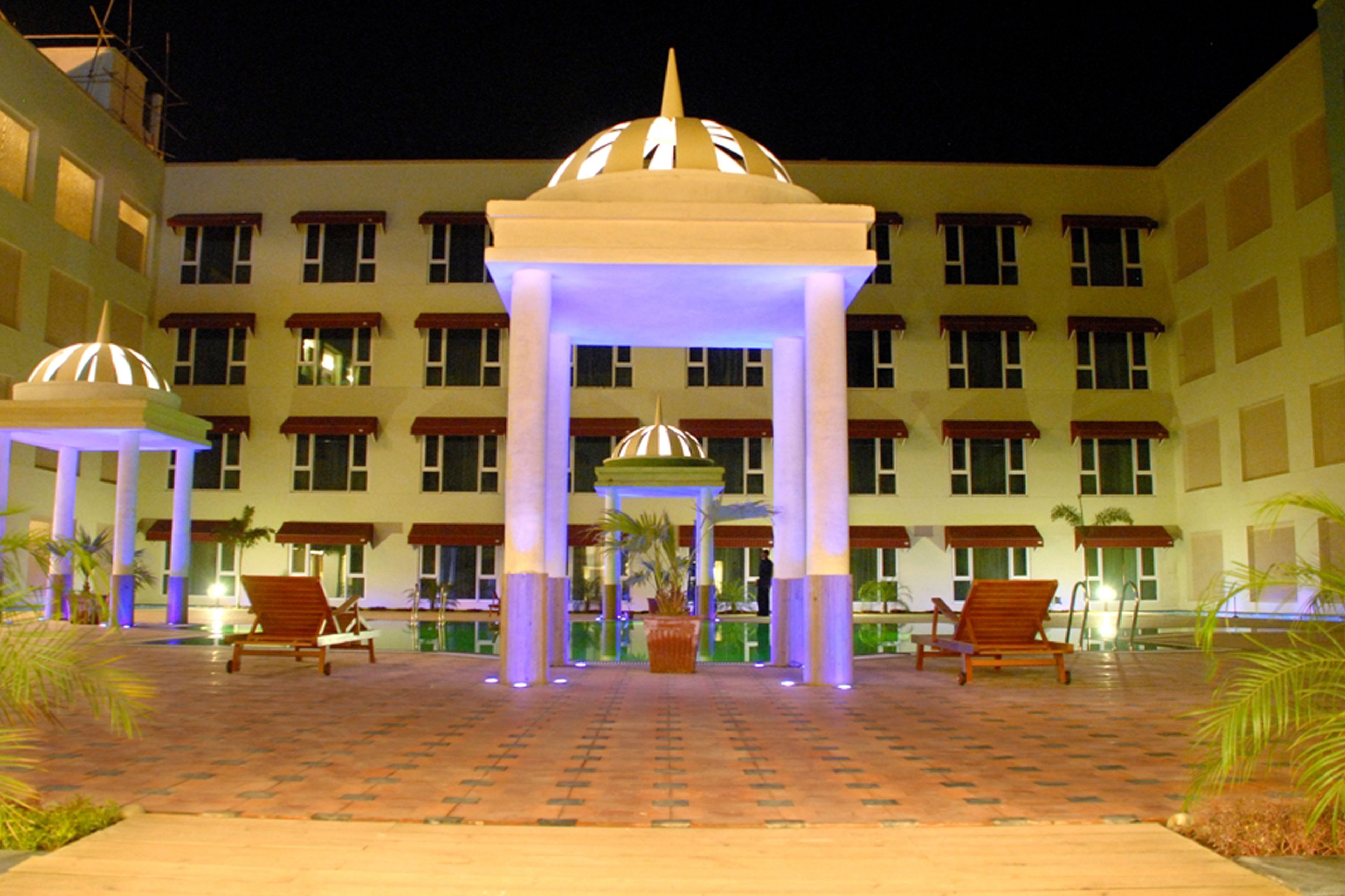 A hotel courtyard with a central gazebo, multiple lounge chairs, and a pool area.