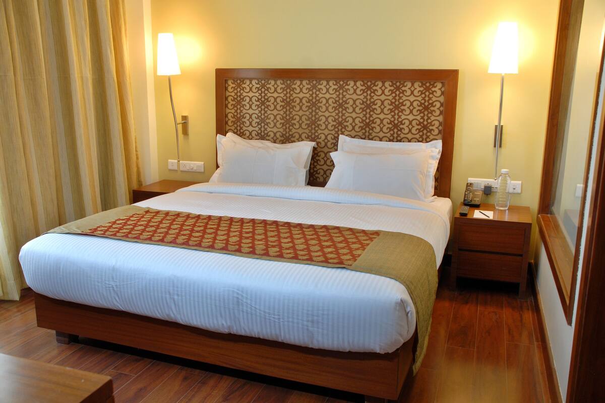 A hotel room with a large bed, wooden headboard, two bedside tables, and two wall-mounted lamps.