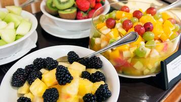Un bufé con varias fuentes de fruta, incluyendo piña, frambuesas, kiwi, fresas y una ensalada de frutas variadas.