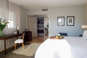 A hotel room with a bed, a desk, a chair, a small table with a tray of food, and a vase with flowers. - Nuss Hotel Buenos Aires Soho (Buenos Aires)