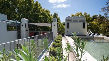 A rooftop pool area with a glass balustrade, potted plants, and a water feature.