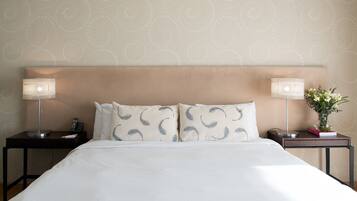 Una cama bien hecha con edredón blanco, dos mesitas de noche con lámparas y un arreglo floral en una de las mesitas.