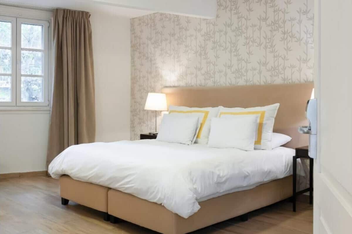 A bedroom with a bed, a nightstand, a lamp, and a window with curtains.