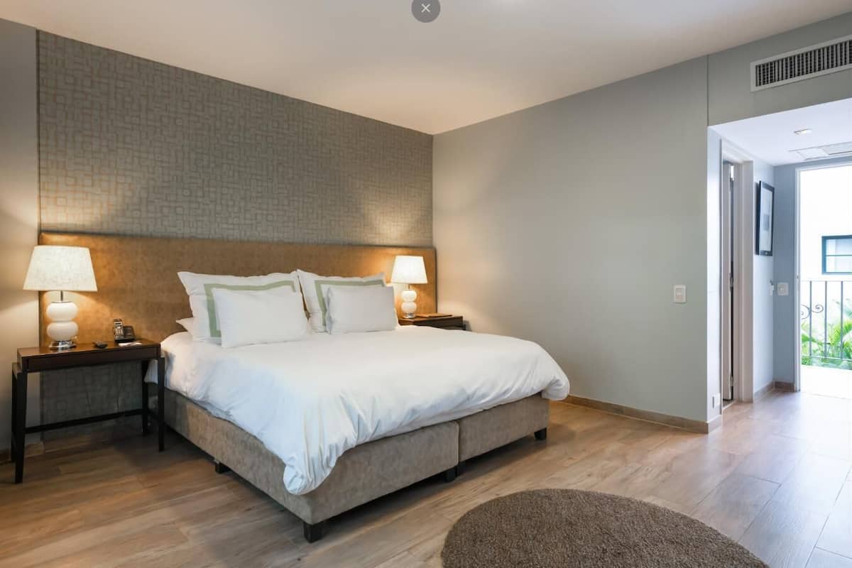 A bedroom with a large bed, two bedside tables with lamps, a patterned wall, and a view of the outdoors.
