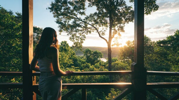 A person standing on a wooden deck overlooking a lush landscape with trees and a distant view of the horizon. - Posada Puerto Bemberg (Puerto Libertad)