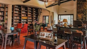 A spacious library with high ceilings and exposed wooden beams, featuring bookshelves, a red armchair, and a dining area with a table and chairs. - Posada Puerto Bemberg (Puerto Libertad)