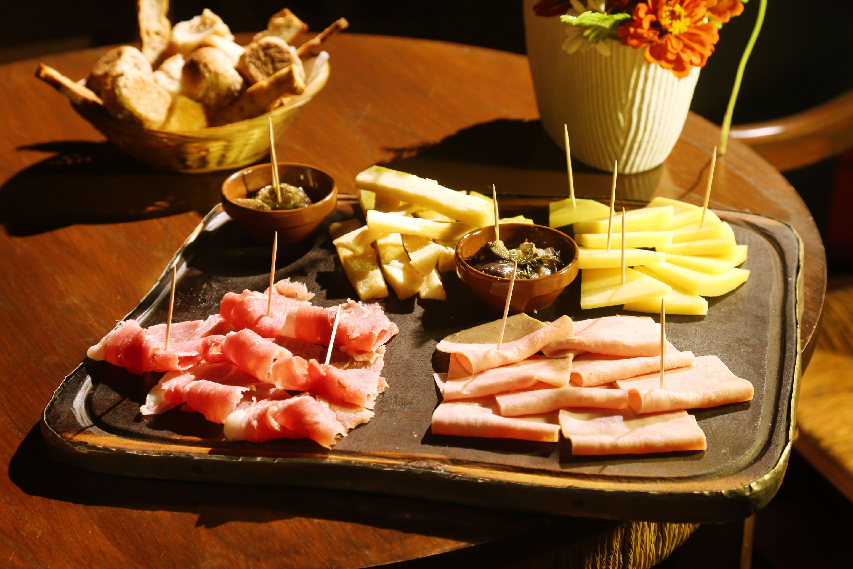 Una tabla de fiambres con diferentes carnes y quesos sobre una bandeja de madera.