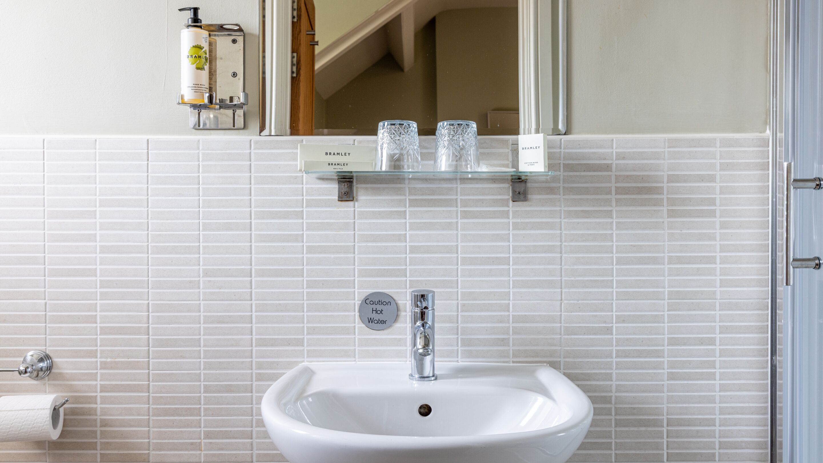 A bathroom with a white sink, a mirror, and a caution sign for hot water.