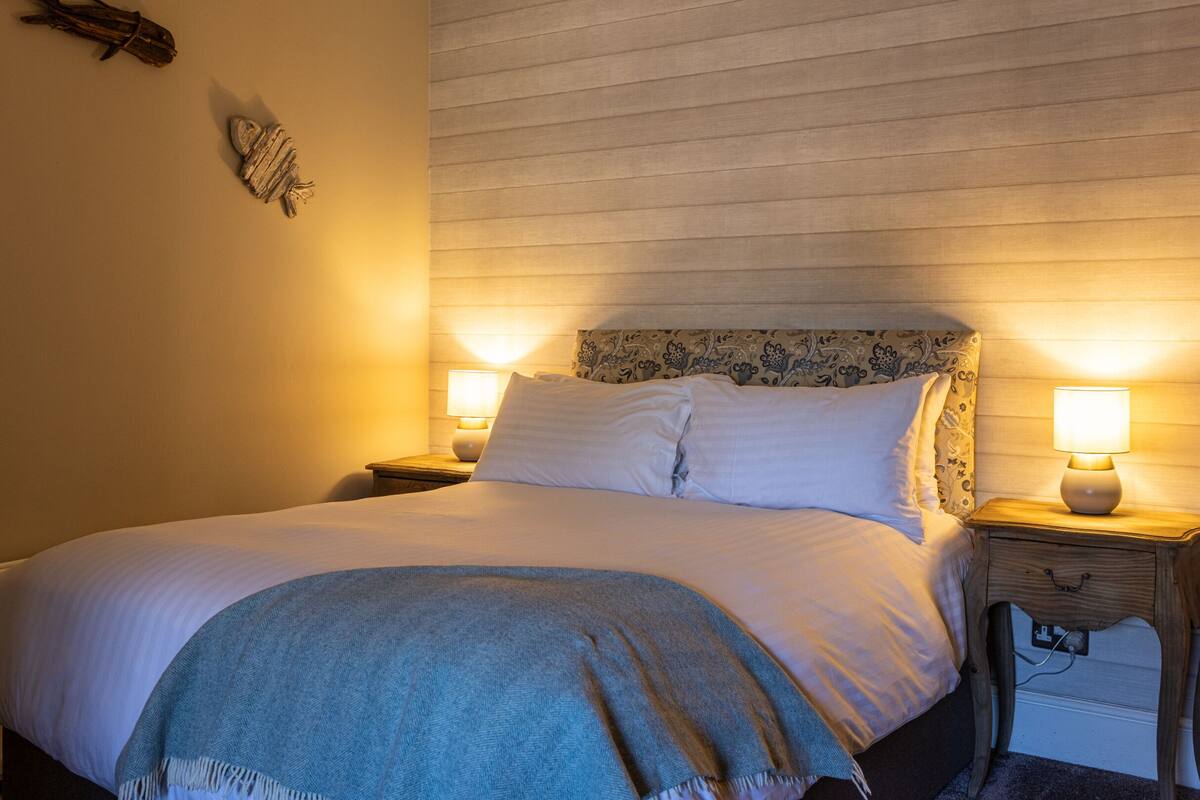 A neatly made bed with two bedside tables, each with a lamp, in a room with wooden paneling on the walls.