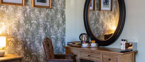 A room with a wooden desk, a chair, a large mirror, and framed pictures on the wall.