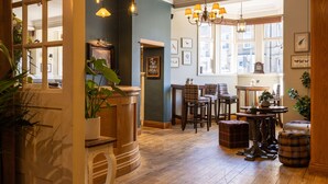 A cozy interior with wooden floors, bar stools, a table with chairs, and framed artwork on the walls. - The Plough (Alnwick)