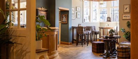 Un intérieur chaleureux avec un plancher en bois, des tabourets de bar, une table avec des chaises et des œuvres d’art encadrées accrochées aux murs.