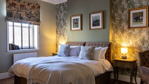 A bedroom with a bed, a window with blinds, a radiator, a nightstand with a lamp, and a chair. - The Plough (Alnwick)