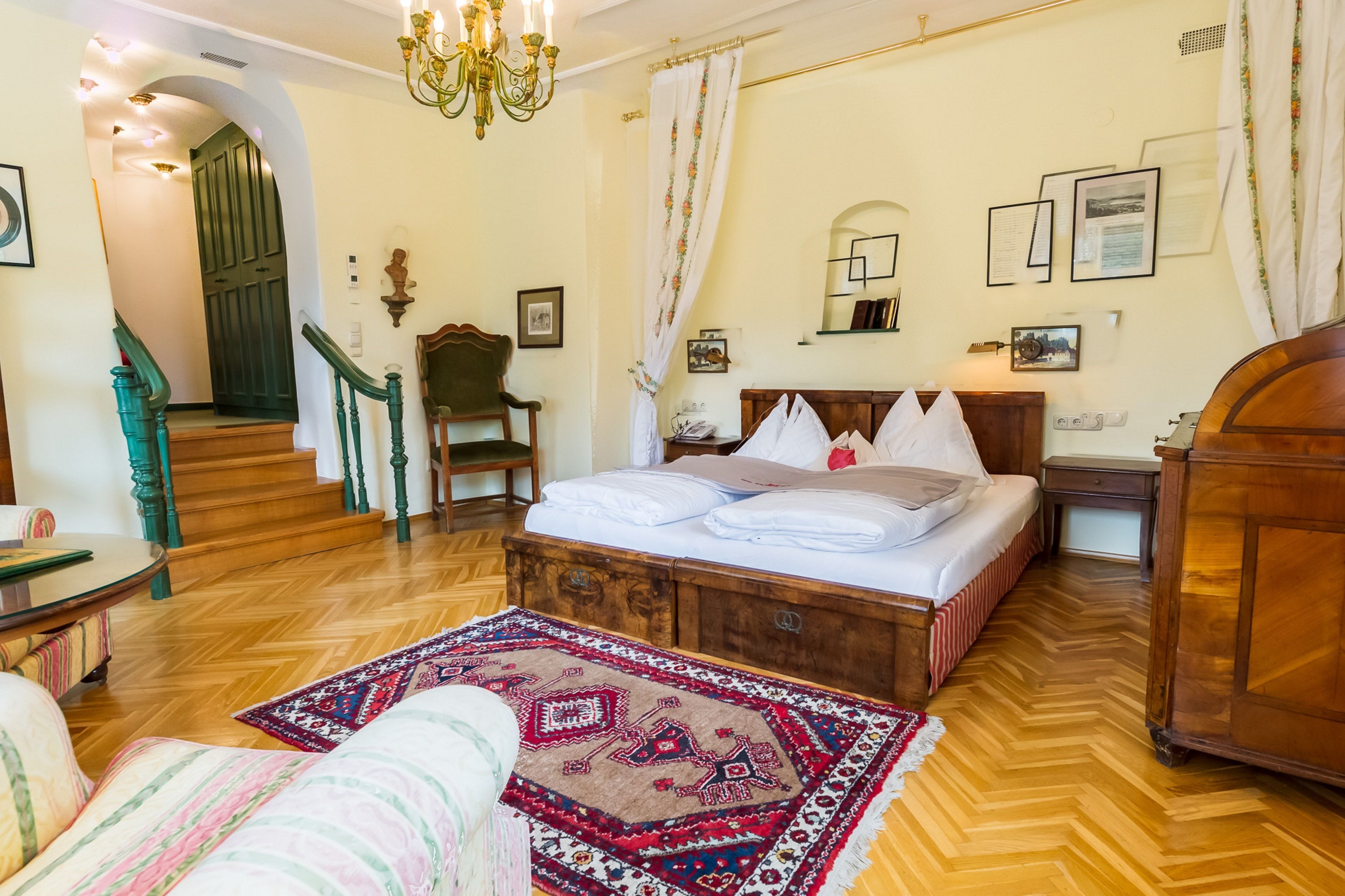 Un dormitorio con cama de madera, una silla, un escritorio, un espejo y una araña.