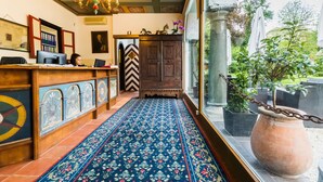 A reception area with a wooden desk, a patterned carpet, and a large window with a view of greenery. - Hotel Schloss Leonstain (Poertschach am Woerthersee)