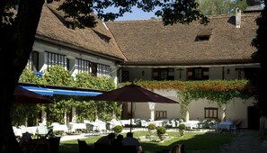 A courtyard with outdoor seating, a covered area, and a building with a tiled roof. - Hotel Schloss Leonstain (Poertschach am Woerthersee)