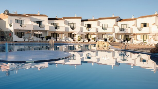 Un hotel con varias edificaciones blancas, una piscina y tumbonas.