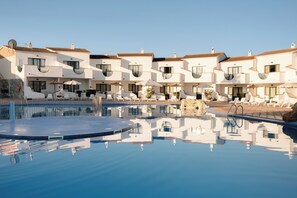Un hotel con varias edificaciones blancas, una piscina y tumbonas.