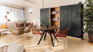 Una sala de estar moderna con una mesa redonda de madera, sillas de mimbre, una estantería y una planta grande en maceta.