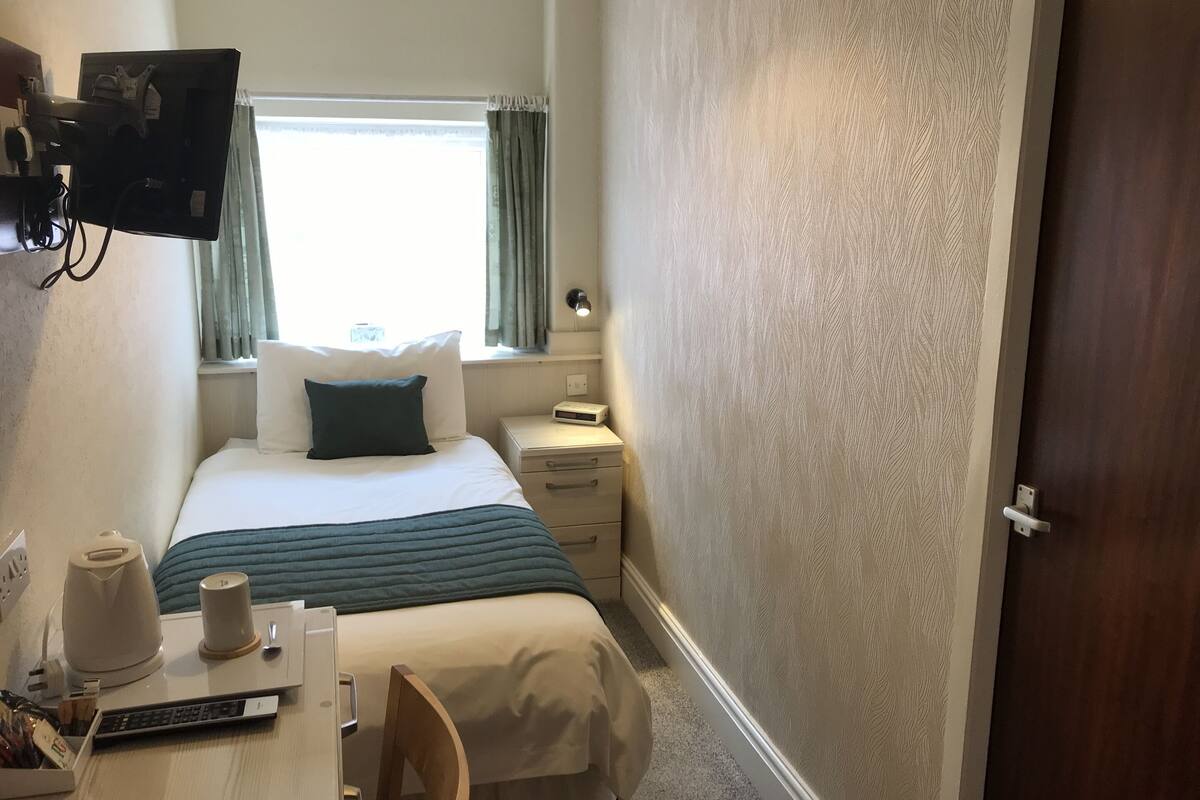 A hotel room with a bed, bedside table, lamp, and a television mounted on the wall.
