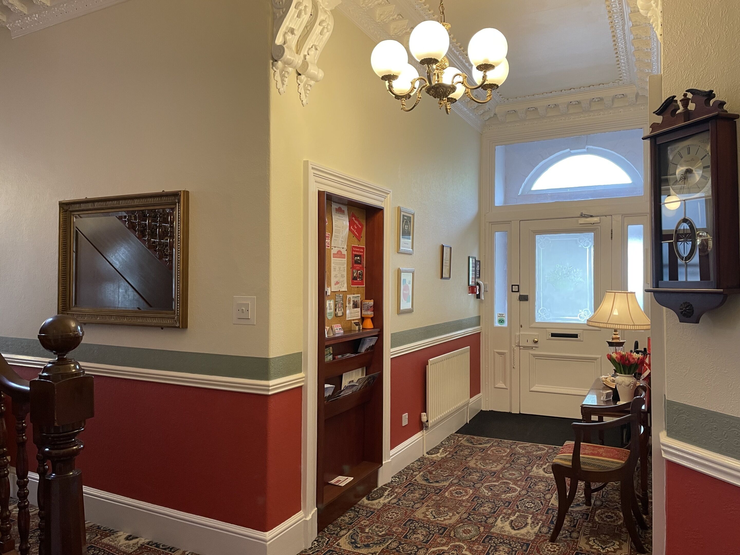 A hallway with a red and white wall, a chandelier, a clock, and a door with a window.