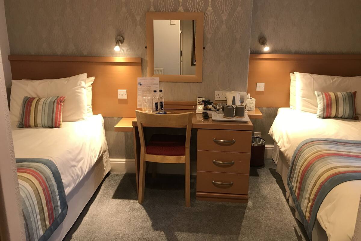 A hotel room with two beds, a desk with a chair, a mirror, and a small table with toiletries.