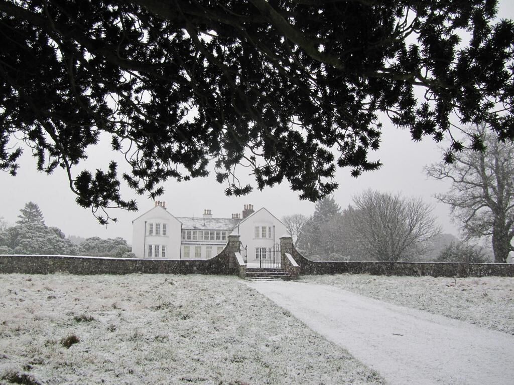 A white building with a symmetrical facade, a central entrance, and a paved driveway leading to it.