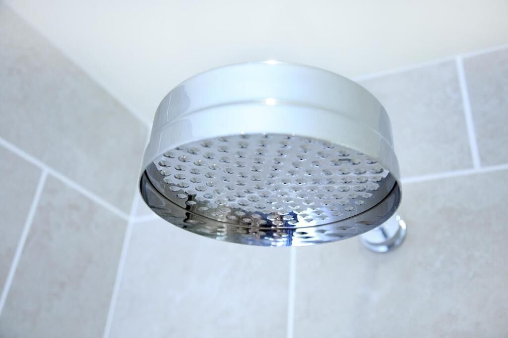 A showerhead with a perforated design, mounted on a wall with a tiled surface.
