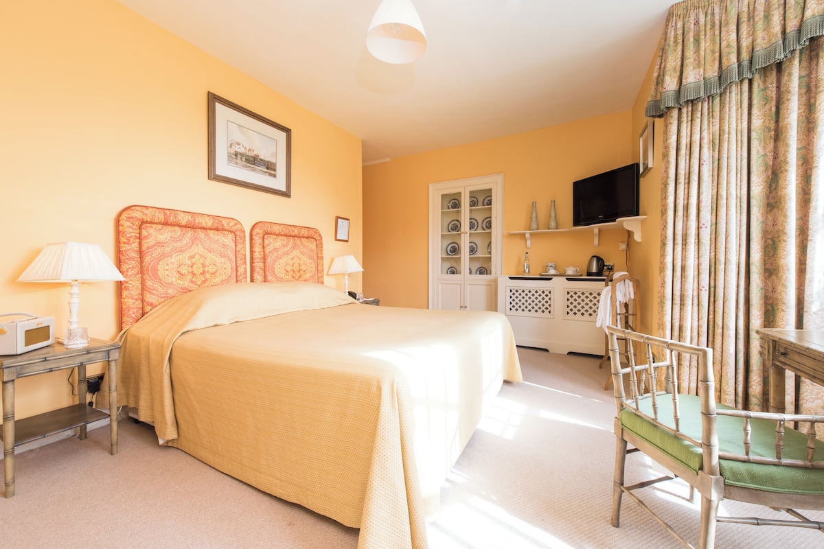 A hotel room with a bed, bedside tables, a chair, a television, and a cabinet with decorative items.